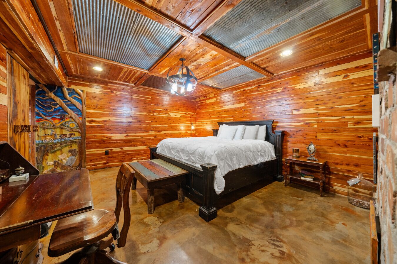 Interior de uma cabana de madeira com uma cama, uma escrivaninha e uma cadeira.