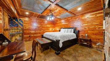 Interior de uma cabana de madeira com uma cama, uma escrivaninha e uma cadeira.