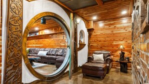 A cozy room with a circular mirror, leather sofa, armchair, and a small table with a lamp. - The Hobbit House, Fantasy comes Home! (Russellville)