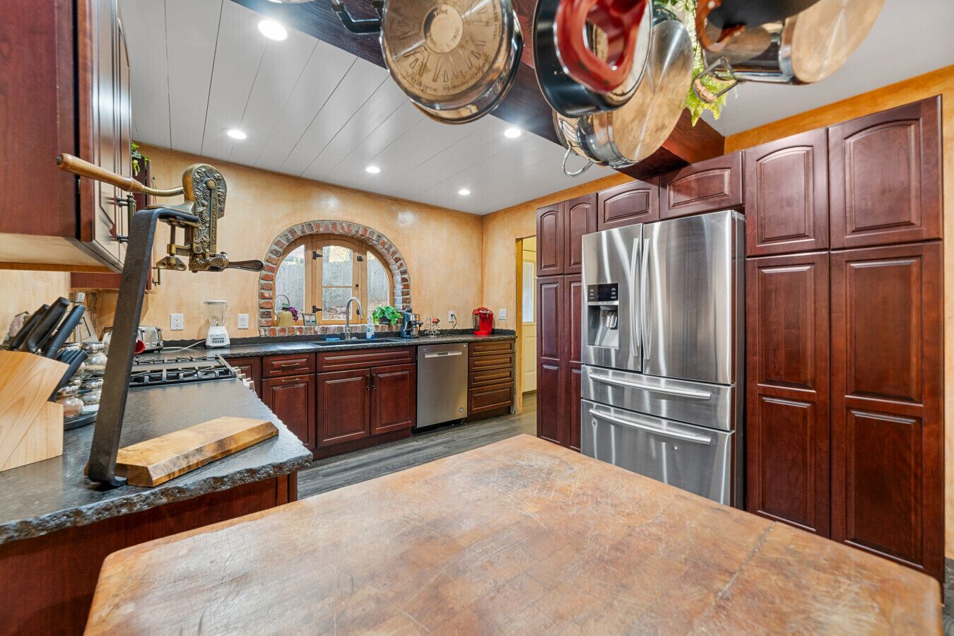 A kitchen with dark wooden cabinets, a stainless steel refrigerator, and a stone countertop.