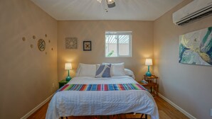 Quarto com cama, duas mesas de cabeceira com luminárias, ventilador de teto, janela e decoração nas paredes.