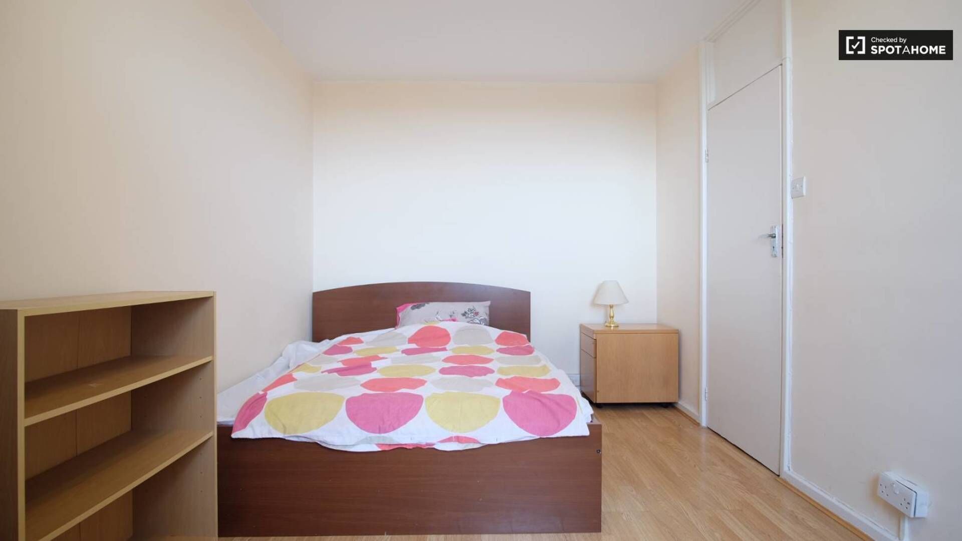 A bedroom with a wooden bed, a nightstand with a lamp, and a wardrobe.
