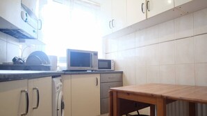 A kitchen with white cabinets, a microwave, a dishwasher, and a wooden table. - 2-bed Apartment in London Woolwich (London)