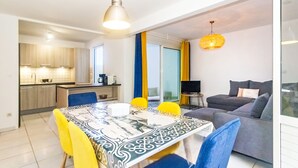 Een moderne woonkamer met een grijze bank, een eettafel met gele stoelen, en een keuken op de achtergrond.