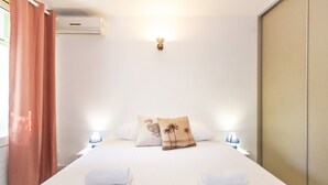 Een netjes opgemaakt bed met twee kussens, een wandlamp en een nachtkastje met een lamp.