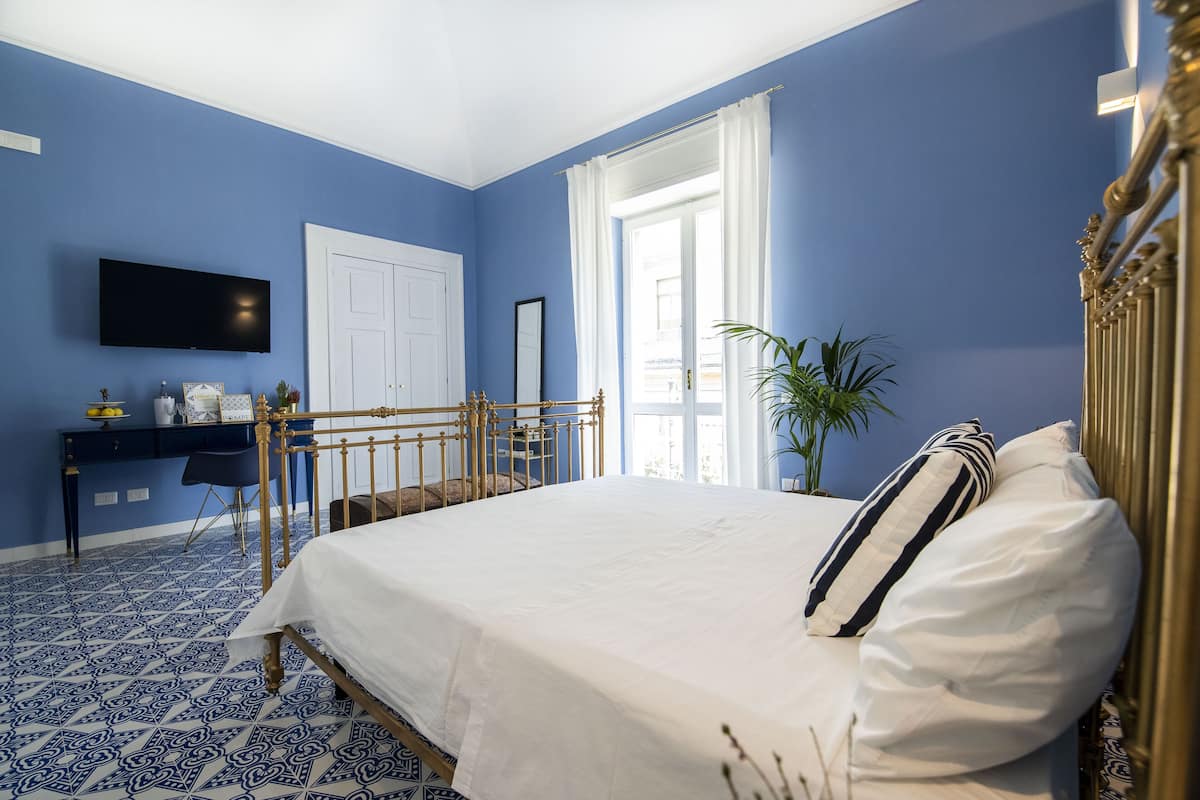 A bedroom with a bed, a desk, a television, and a window with curtains.