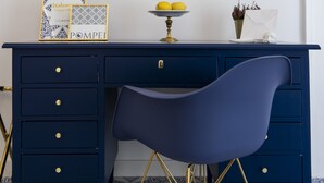 A dark blue desk with gold handles, a flat-screen TV above it, a blue chair with gold legs, and patterned floor tiles.