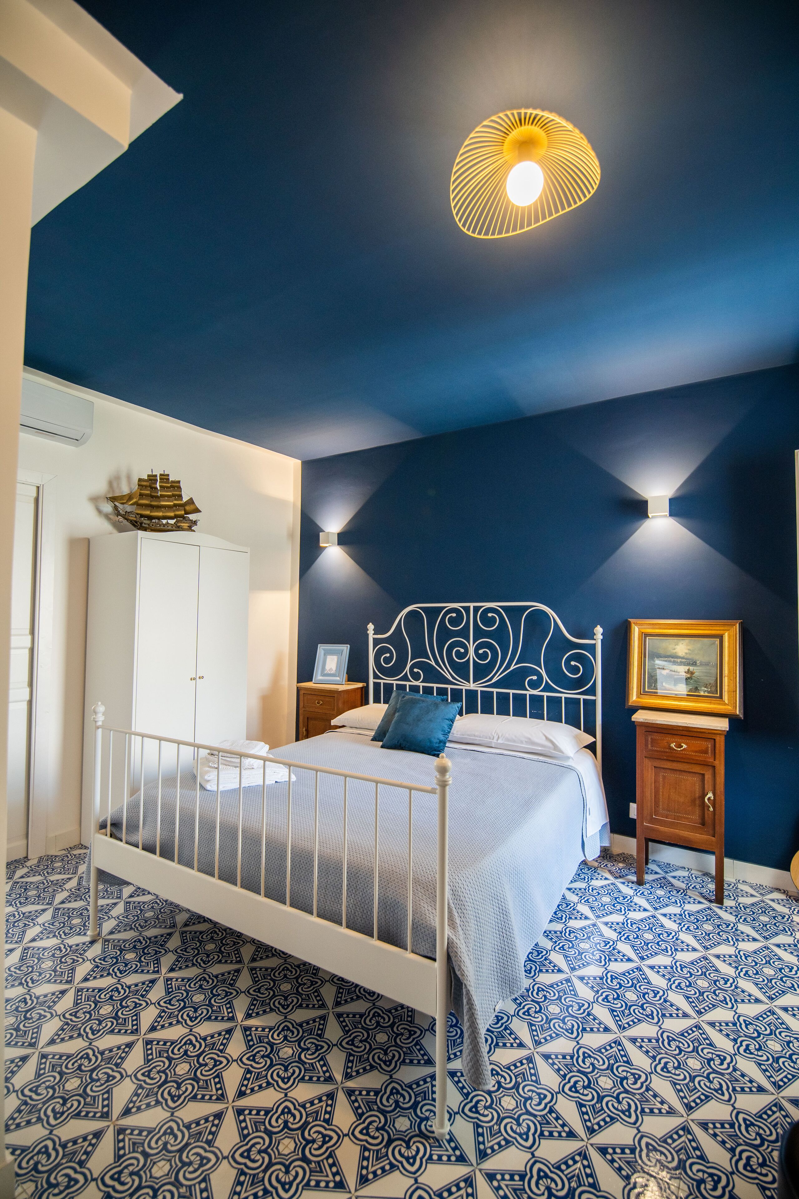 Un dormitorio con cama, armario, mesita de noche y lámpara de pared.