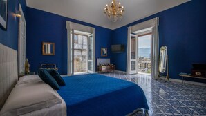 A bedroom with a large bed, a chandelier, a dresser, and a view through the open door.