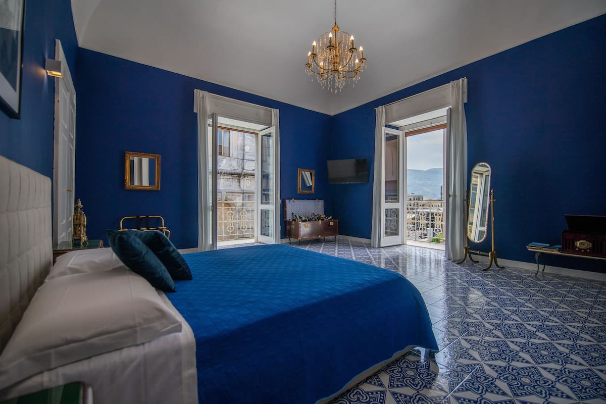 A bedroom with a large bed, a chandelier, a dresser, and a view through the open door.