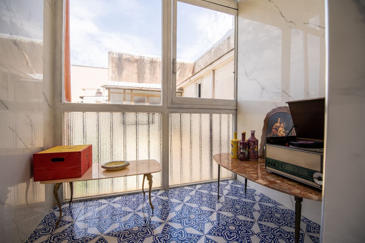 A small room with a tiled floor, a window, a table with a bowl, and a vintage radio.