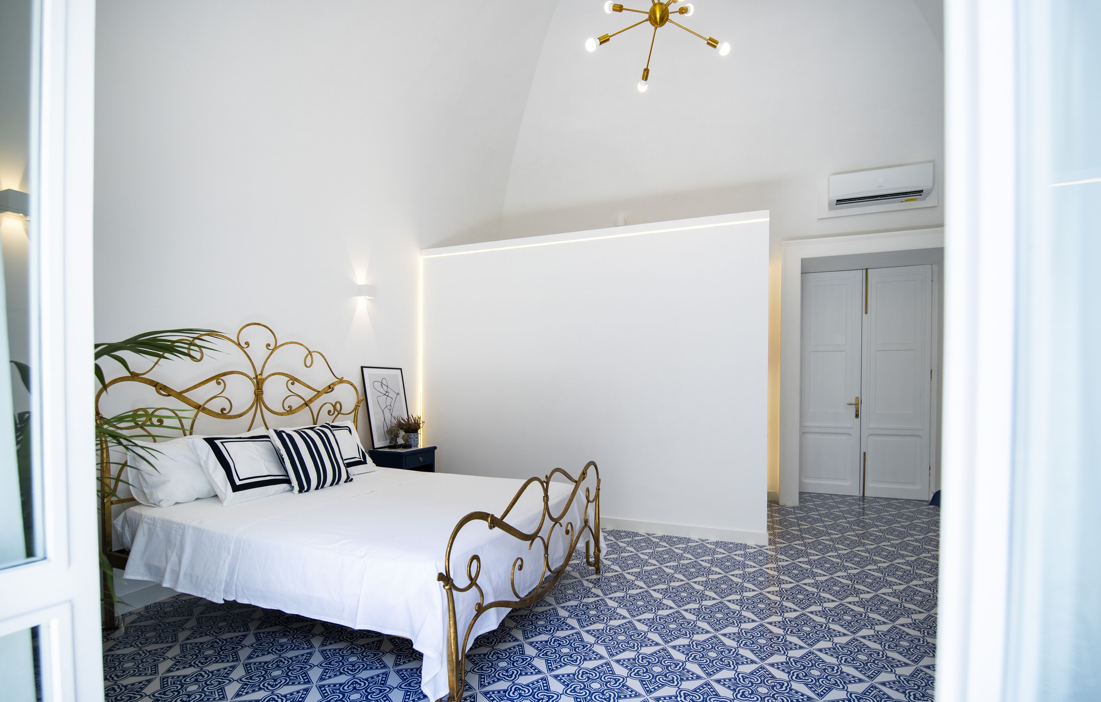 Quarto com cama, mesa de cabeceira, luminária na parede e ventoinha no teto.