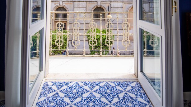 A view from a room with a patterned floor through a glass door leading to a balcony.