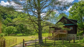 A rustic cabin with a wooden staircase and a fenced yard. - Woodsy Retreat with Hot Tub | Dogs Welcome | On River Time (Lansing)