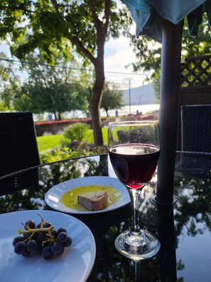 A table with a glass of red wine, a plate with a slice of bread and a small bowl of yellow sauce, and a plate with grapes. - LAKEFRONT- 3 bdrm Townhome #108 Amazing Osoyoos Chris - casadeloro108@gmail.com (Osoyoos)