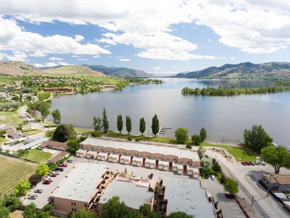 A hotel with a flat roof, parking lot, and a view of a lake and mountains. - LAKEFRONT- 3 bdrm Townhome #108 Amazing Osoyoos Chris - casadeloro108@gmail.com (Osoyoos)