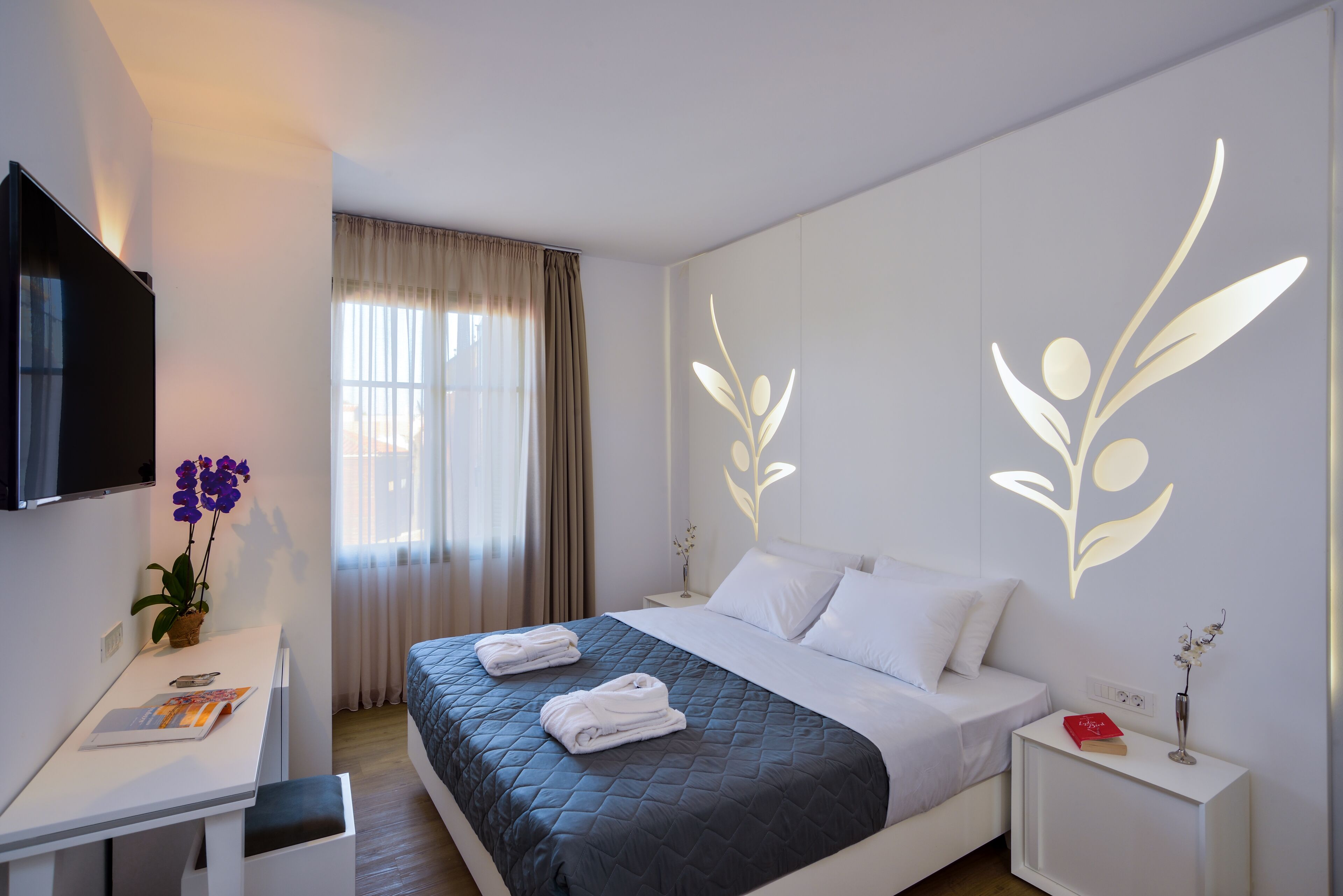 Una habitación de hotel con cama, escritorio, televisor y ventana con cortinas.