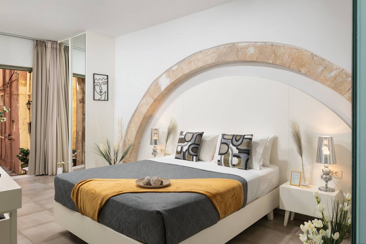 Een moderne slaapkamer met een groot bed, een stenen boog, een nachtkastje met een lamp en uitzicht op het omliggende landschap.