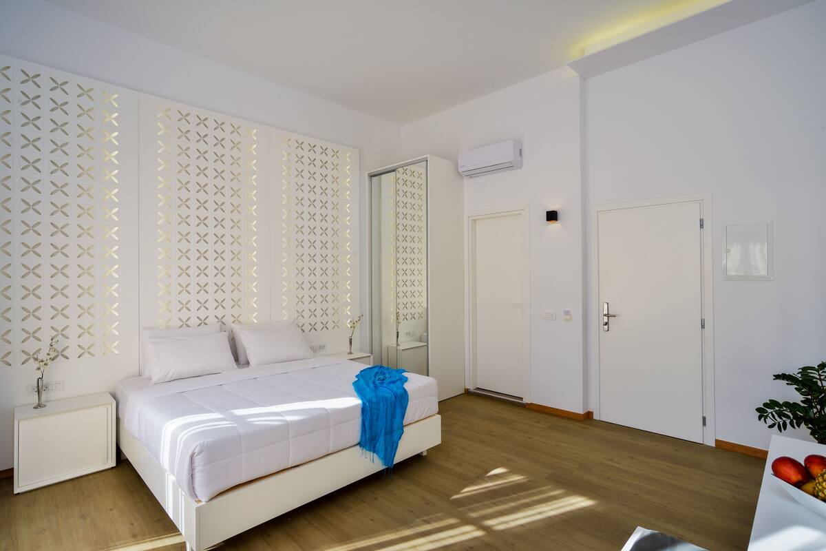 Een moderne slaapkamer met een bed, nachtkastjes, een spiegel en een deur.