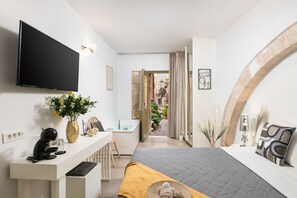 Un dormitorio moderno con una televisión de pantalla plana, un escritorio con cafetera, una cama con cubrecama acolchado y un baño visible a través de una puerta abierta.