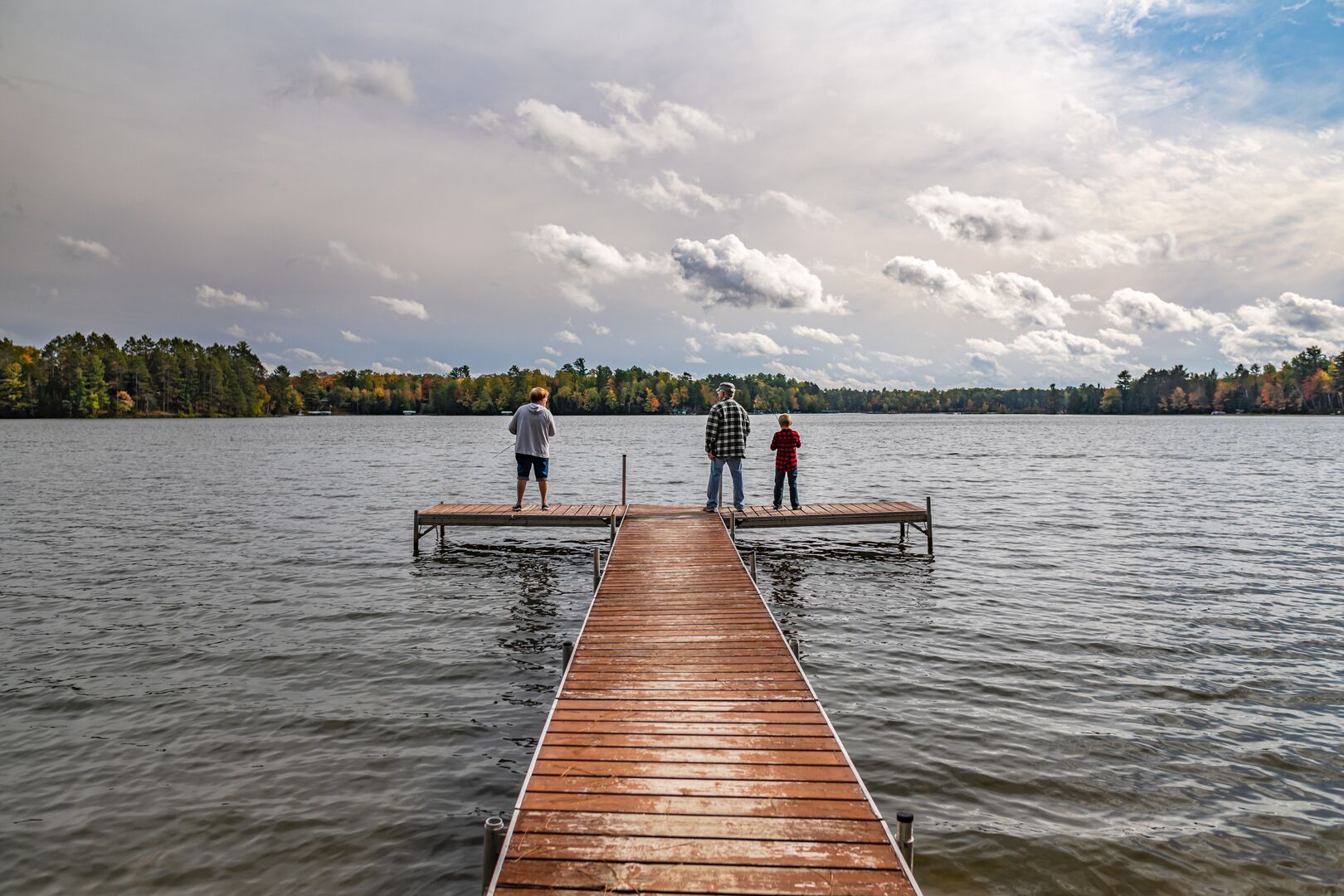Un muelle de madera que se adentra en un lago tranquilo, con una orilla boscosa al fondo.