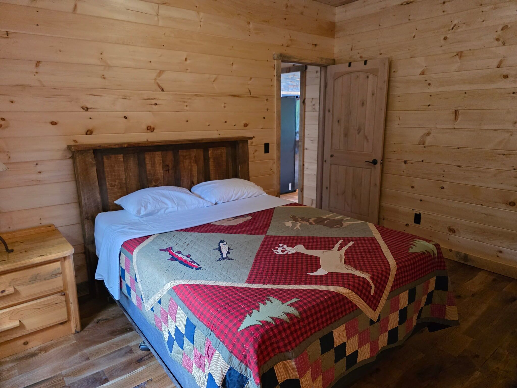 Una camera in una baita di legno, con un letto, un comodino e una porta.