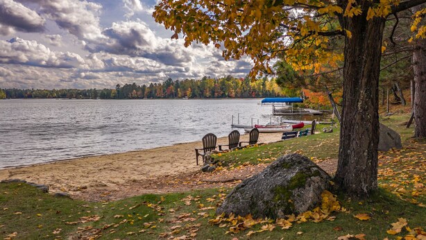 A lakeside view with a dock, chairs, and a covered area. - Brand new pet friendly vacation home with private dock and firepit! (St. Germain)