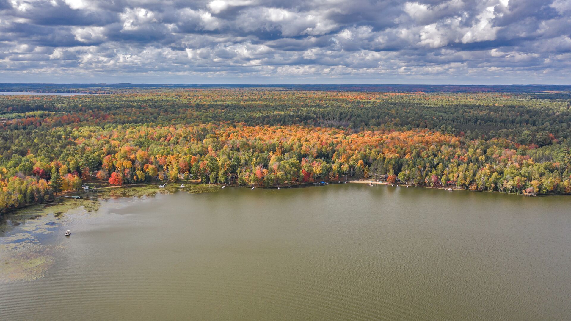 An aerial view of a lake surrounded by dense forest with autumn foliage.