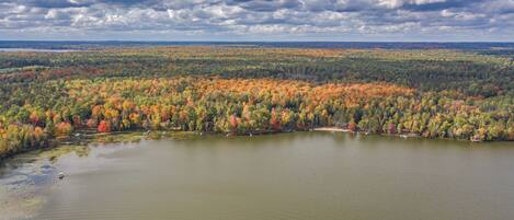 An aerial view of a lake surrounded by dense forest with autumn foliage.