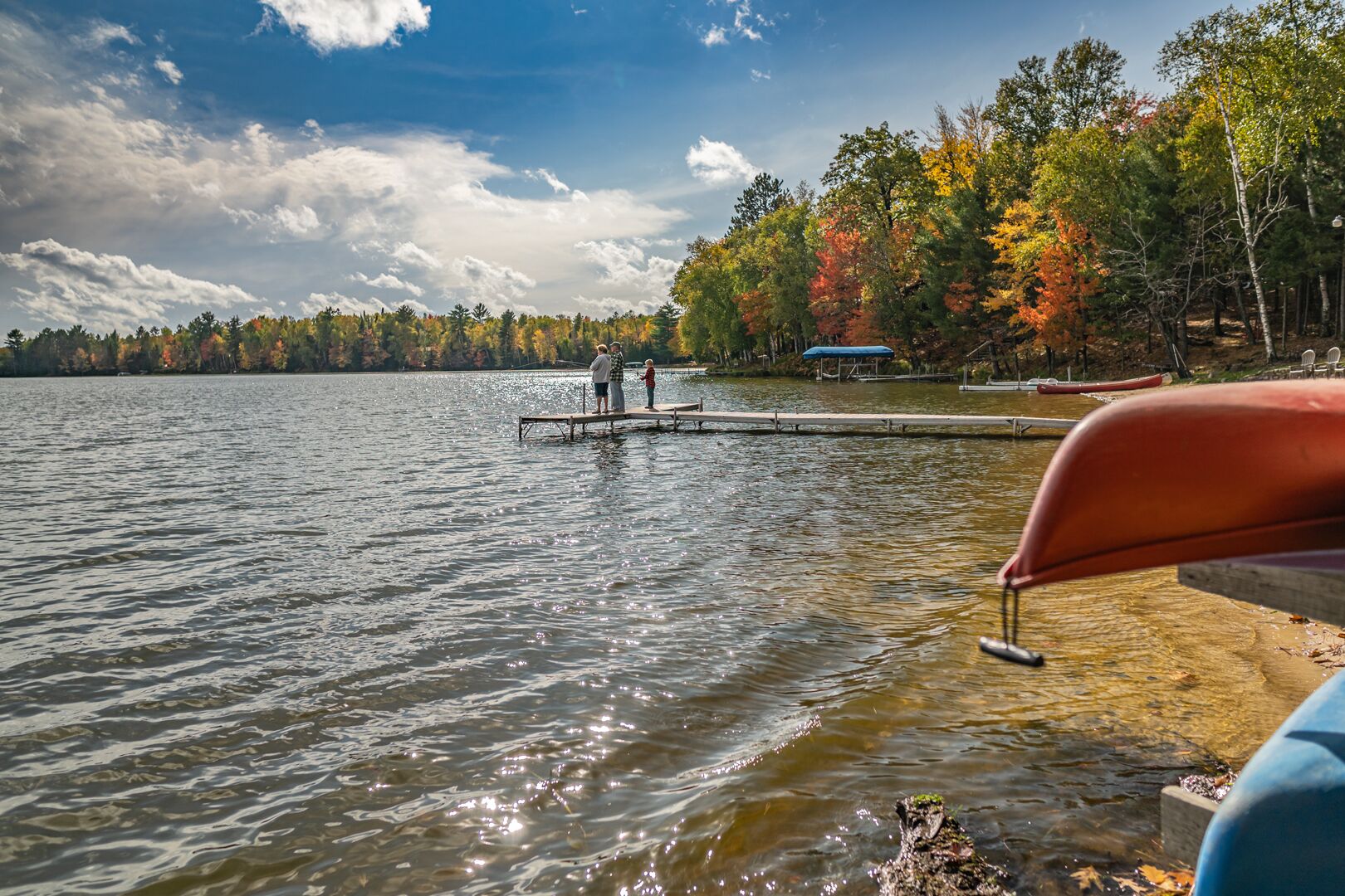 A lake with a dock extending into the water, surrounded by trees with autumn foliage.