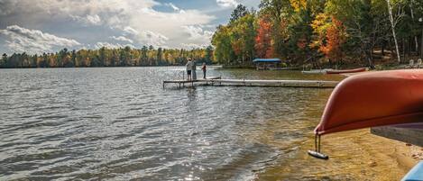 A lake with a dock extending into the water, surrounded by trees with autumn foliage.