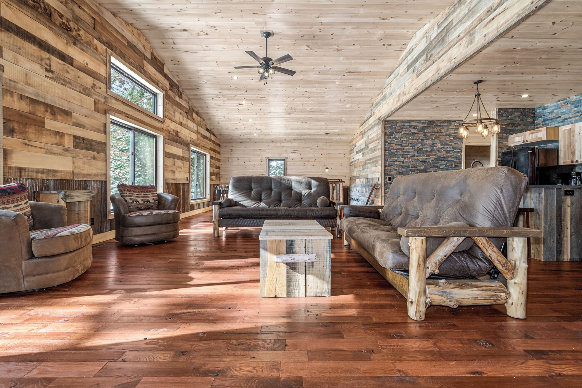 Un salon spacieux avec des murs et des planchers en bois, un grand canapé, une table basse et un ventilateur de plafond.