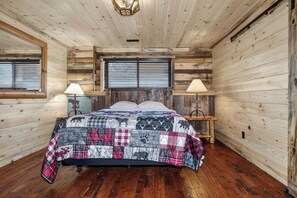 Un dormitorio tipo cabaña de madera con una cama, dos lámparas de noche y un ventanal con persianas.