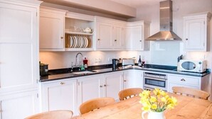 Une cuisine avec des armoires blanches, une table à manger en bois et une hotte de cuisinière en acier inoxydable.