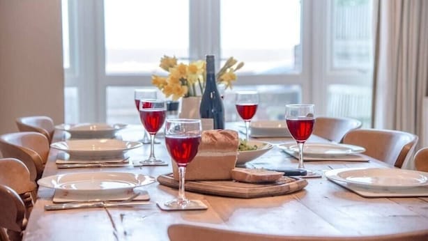 Une table à manger dressée avec des assiettes, des verres et une bouteille de vin, et un vase rempli de fleurs jaunes placé au centre.