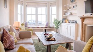 Un salon chaleureux avec un canapé, une table basse en bois sur laquelle sont disposés des en-cas, une cheminée et une bibliothèque.