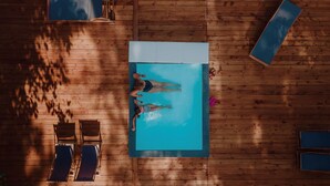En vy från ovan av ett trädäck med en pool, två solstolar och ett överbyggt område.