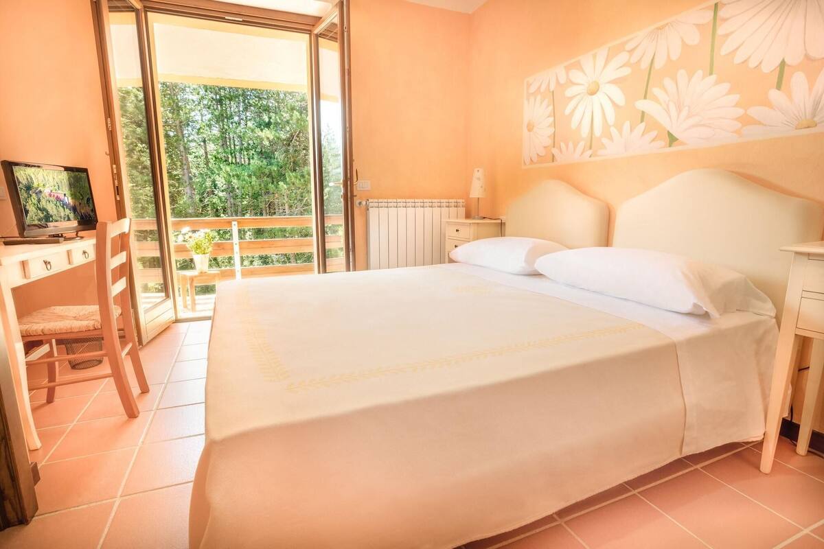 Une chambre avec un lit, une télévision, un bureau et un balcon donnant sur un espace verdoyant.