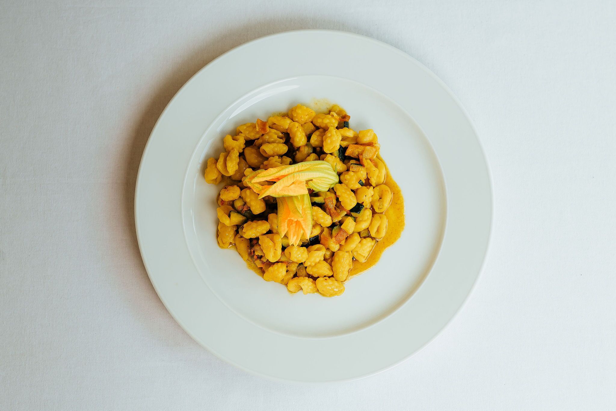 Un plato de pasta amarilla con vegetales sobre un plato blanco.