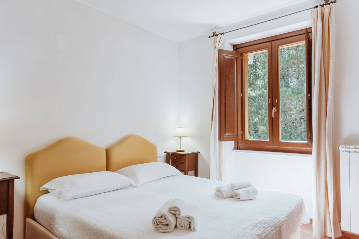 Un lit bien fait, avec des draps blancs et des serviettes pliées, une lampe de chevet et une fenêtre avec des rideaux.