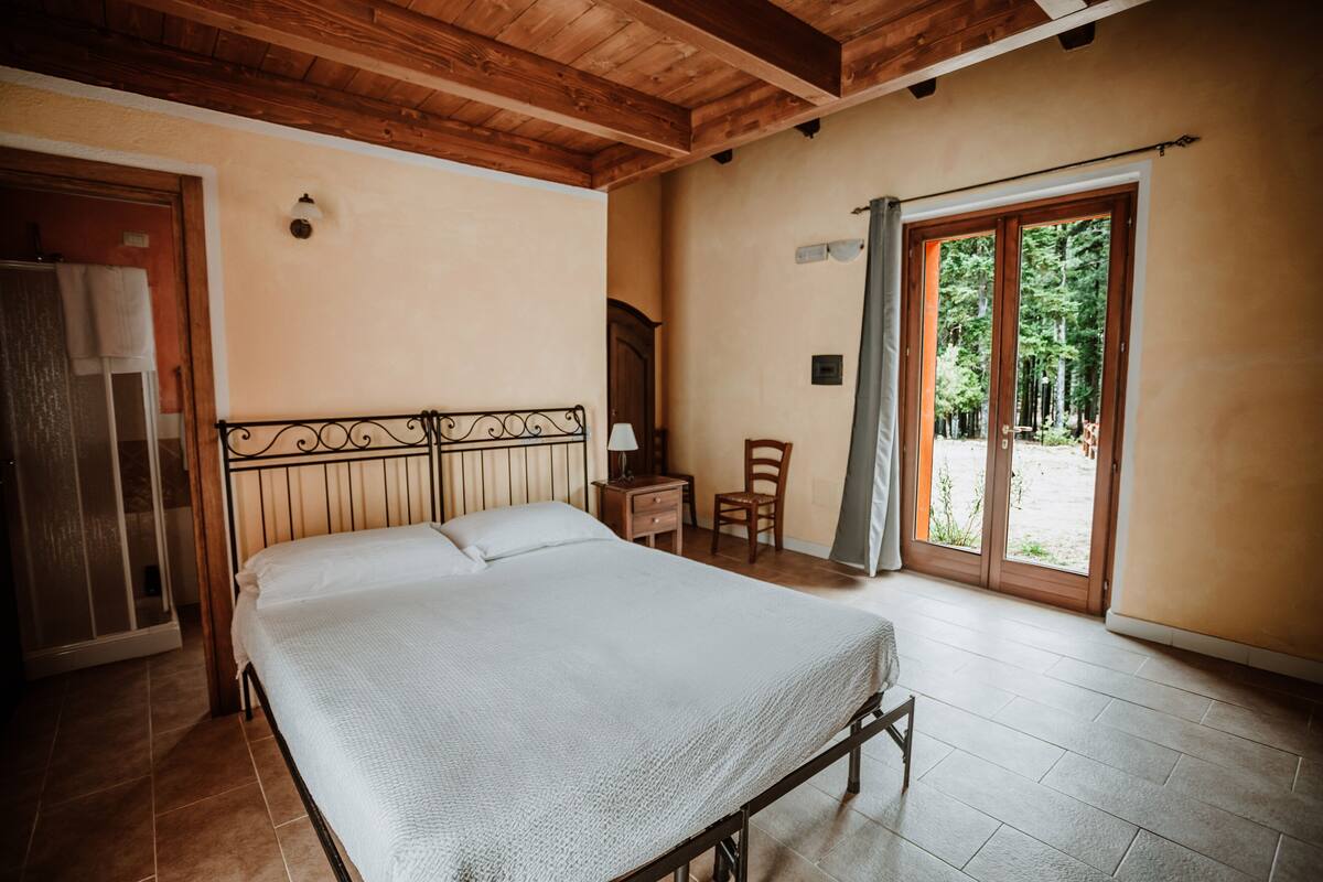 Une chambre à coucher comprenant un lit, une tête de lit en bois, une table de chevet, une chaise et une porte-fenêtre coulissante donnant sur un espace extérieur.