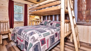 Dormitorio de cabaña de madera con cama, cabecera de madera y ventana con vistas a árboles.