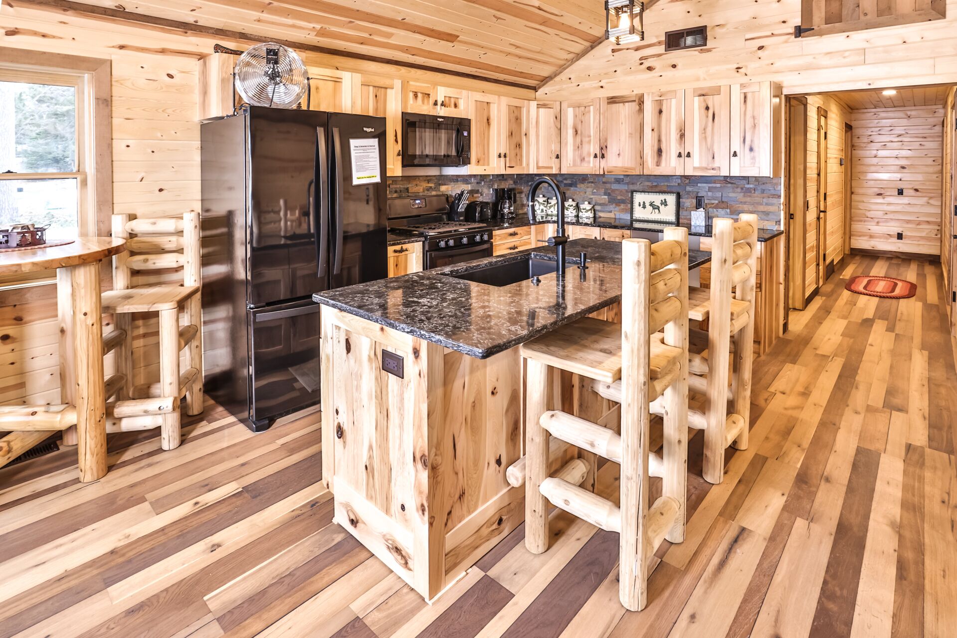 Cocina de cabaña de madera con una isla central, taburetes de bar de madera, refrigerador, estufa y pileta.