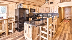 Cocina de cabaña de madera con una isla central, taburetes de bar de madera, refrigerador, estufa y pileta.