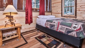 Habitación de cabaña de madera con una cama, una lámpara con forma de alce y vista a los árboles por una ventana.