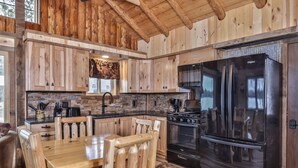 Cocina tipo cabaña de madera con comedor, salpicadero de piedra y un refrigerador negro grande.