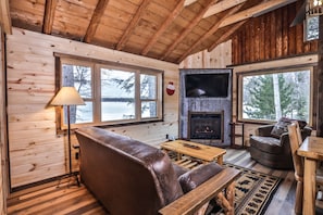 L’intérieur d’un chalet chaleureux, avec un canapé en cuir, une table en bois et une cheminée.