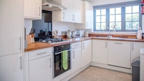 A modern kitchen with white cabinets, a wooden countertop, and a window providing natural light. - 3 Oaks Court, Thorpeness (Leiston)