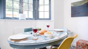 A dining area with a round table, chairs, a potted plant, a painting, and a window with a view. - 3 Oaks Court, Thorpeness (Leiston)