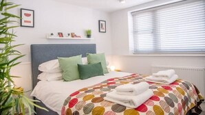 A neatly made bed with a colorful polka dot bedspread, a grey headboard, and a bedside shelf with small decorative items.